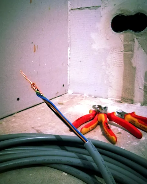 Installatiekabel met gestripte aders en tangen in een ruimte die verbouwd wordt